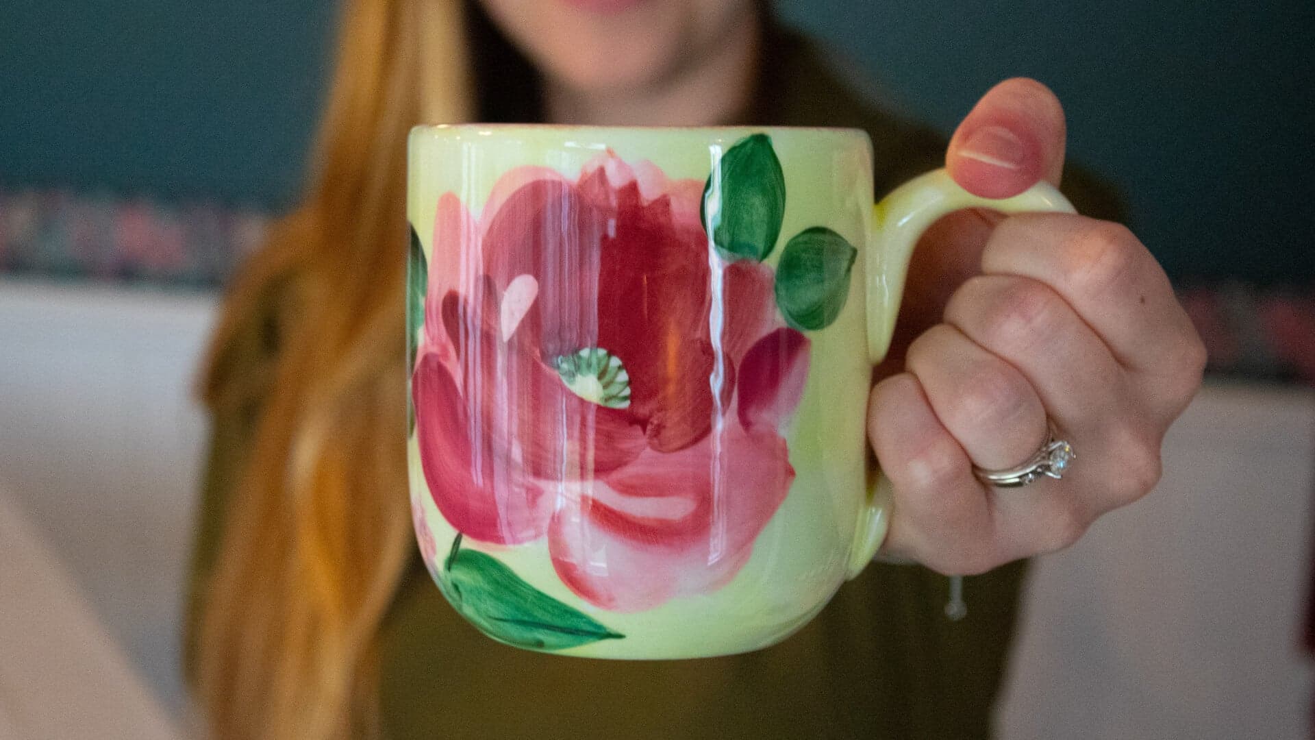 A person holds a floral-painted mug against a colorful backdrop.