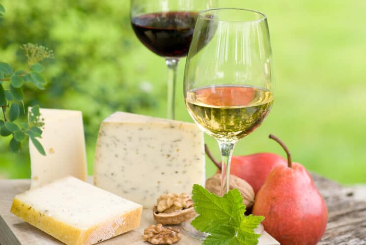 A selection of cheeses, pears, walnuts, and glasses of red and white wine on a wooden surface.