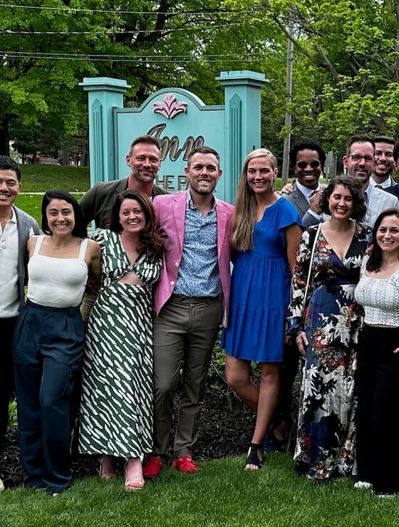 A group of smiling people dressed up on the grass in front of a sign that says Inn at the Park