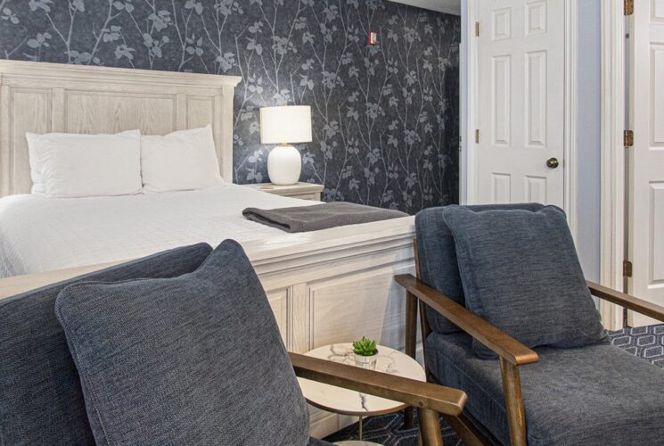 two blue chairs and queen bed against a blue/grey wall papered wall