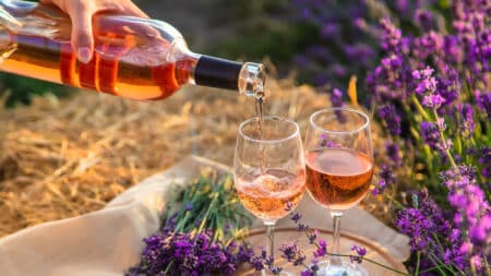 Someone pouring rose wine into 2 wine glasses, with purple flowers around them.