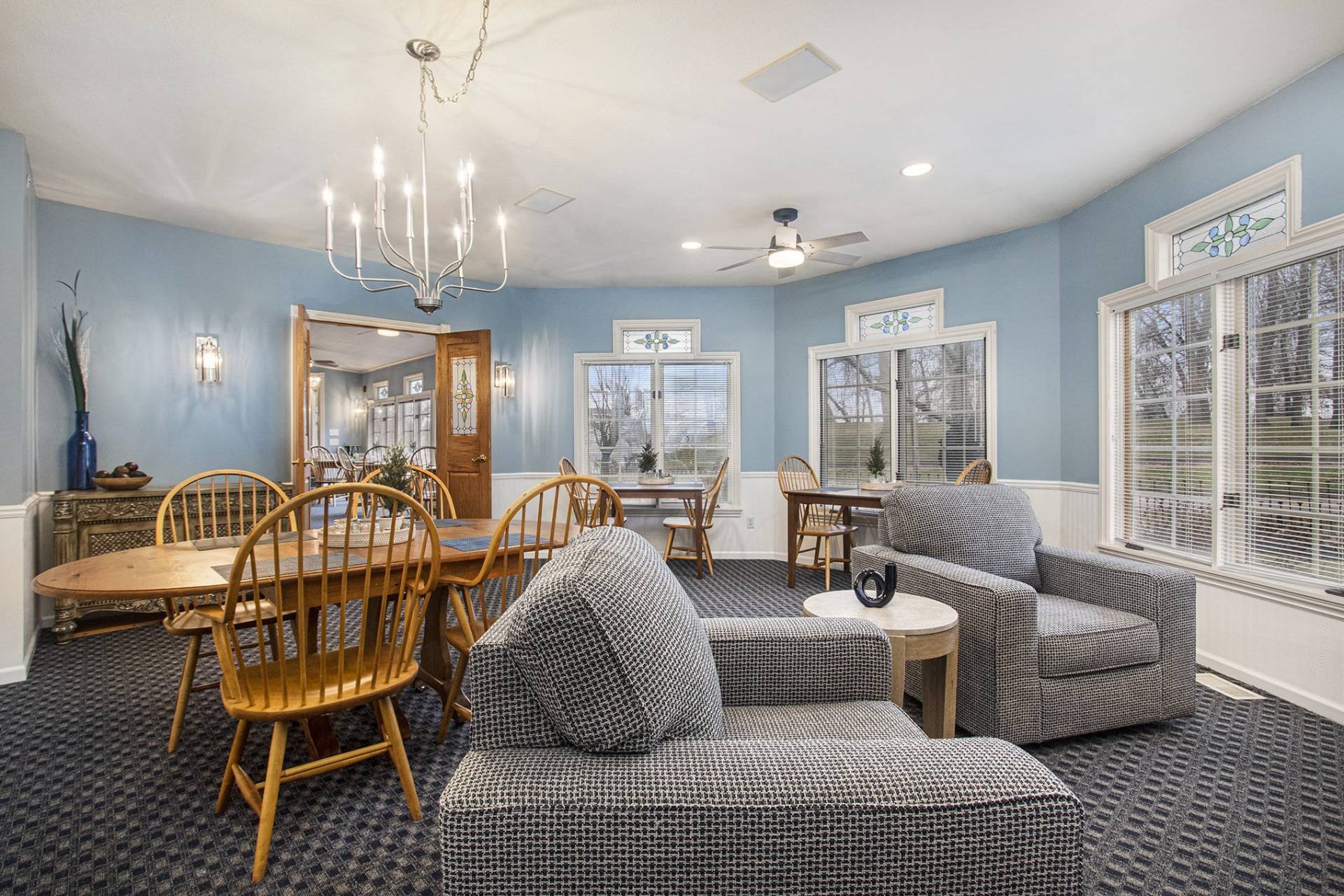 dining room with large chandelier, wooden table and chairs and two blue swivel upholstered chairs