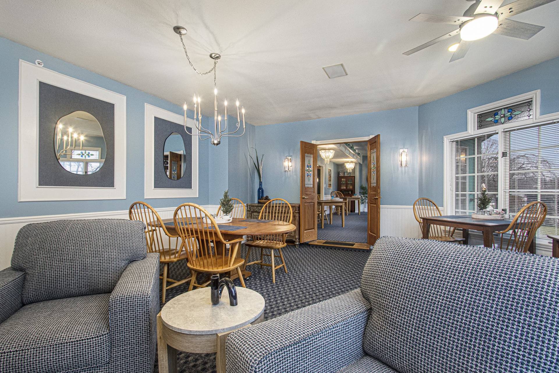 dining room with large chandelier, wooden table and chairs and two blue swivel upholstered chairs